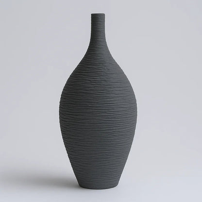 Tall charcoal ceramic vase with a textured tapered body and narrow neck against a grey background