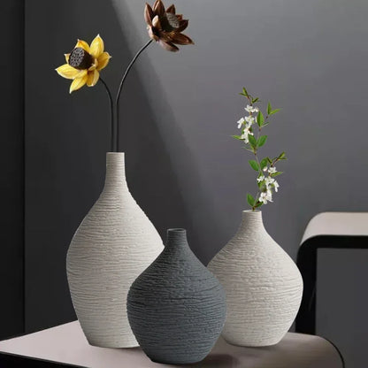 White and charcoal textured vases in two sizes arranged with flowers on a table against a dark wall