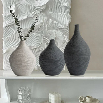 White and charcoal textured narrow-neck vases displayed on a shelf in front of a sculptural wall decoration