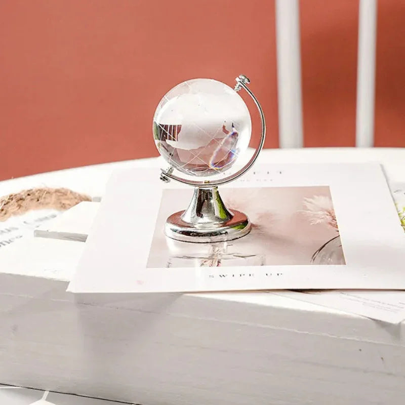 Transparent decorative world map globe on a silver-coloured stand, displayed on a white table