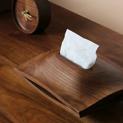 Walnut wood tissue box cover with white tissues on a wooden surface beside a small clock.