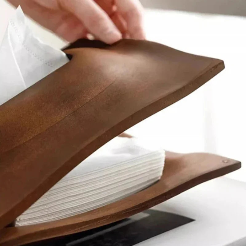 Close-up of a hand lifting the walnut wood tissue box cover lid above a stack of folded tissues.