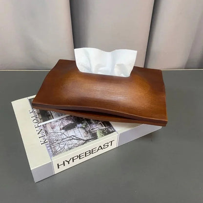 Walnut wood tissue box cover with white tissues, displayed on a magazine on a grey table.