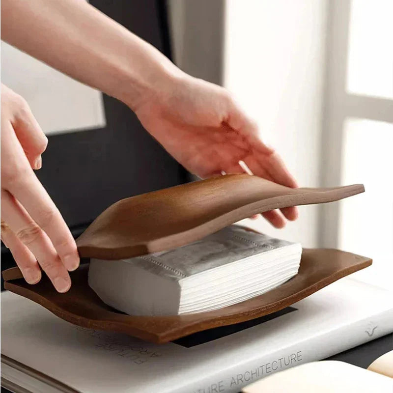 Hands lifting the curved top of a walnut wood tissue box cover to reveal the folded tissues inside.