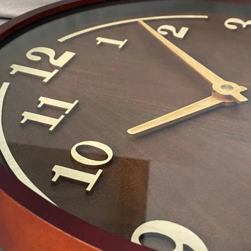 Close-up of the walnut wall clock showing the gold-coloured hands and raised hour numerals.
