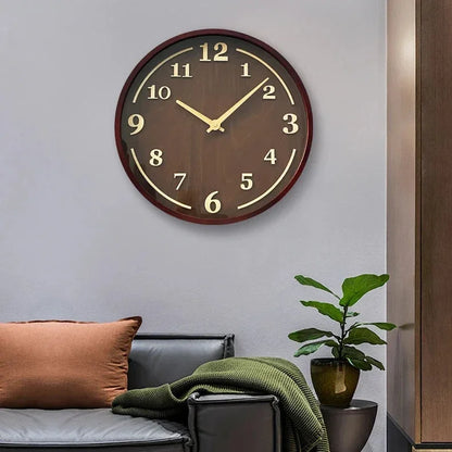 Walnut wall clock above a dark sofa with cushions, a green throw and a potted plant.