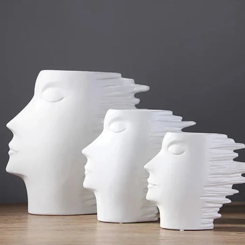 Three white face-shaped ceramic vases in different sizes displayed together on a wooden table.