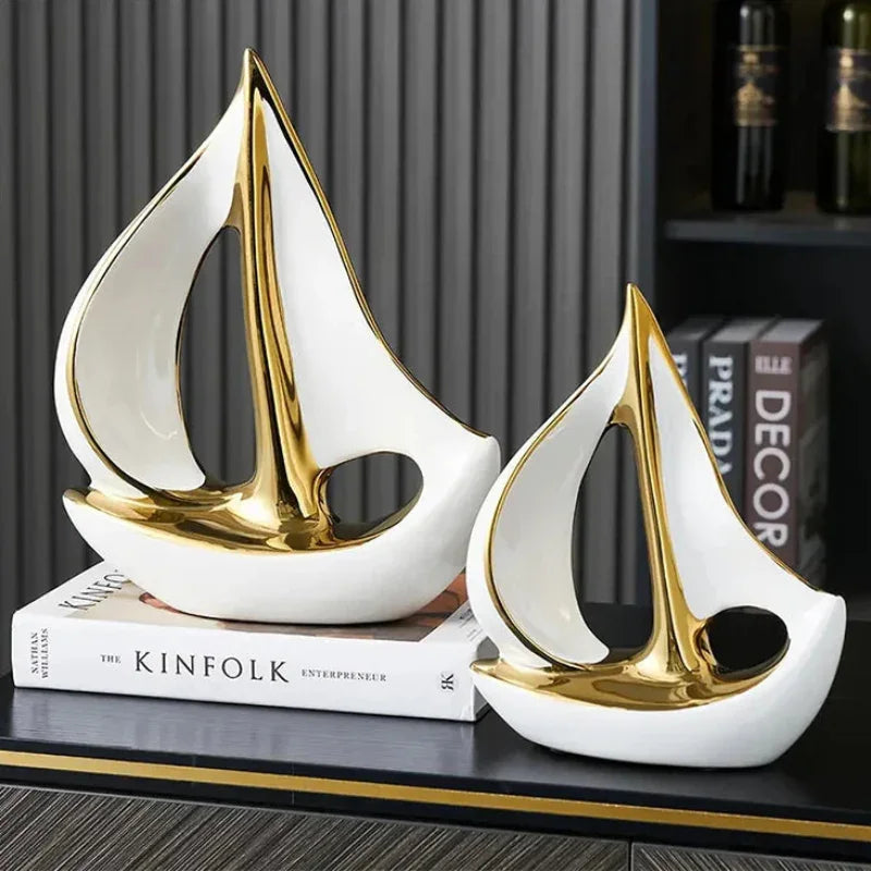 Large and small white sailboat sculptures with gold-coloured details displayed beside stacked books