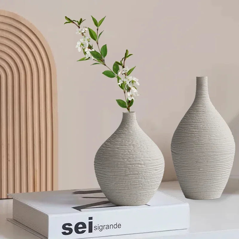 Two white textured ceramic vases with narrow necks, one holding flowering stems, displayed on stacked books