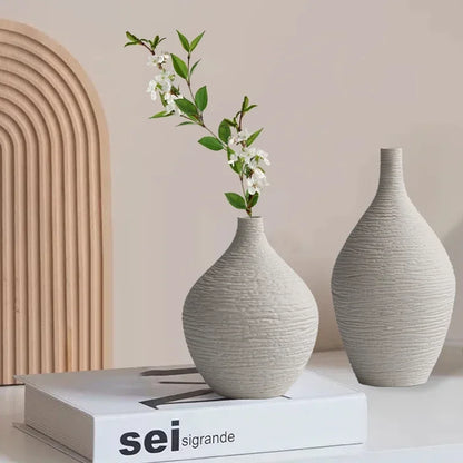 Two white textured ceramic vases with narrow necks, one holding flowering stems, displayed on stacked books