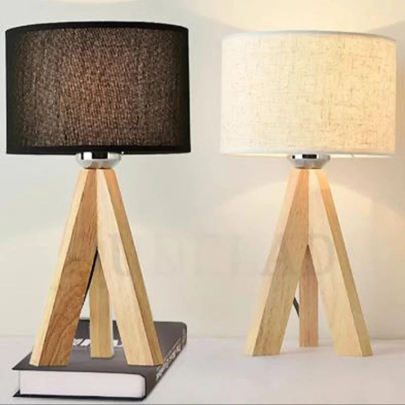 Wooden tripod table lamps with black and cream cylindrical shades, displayed together on a table.